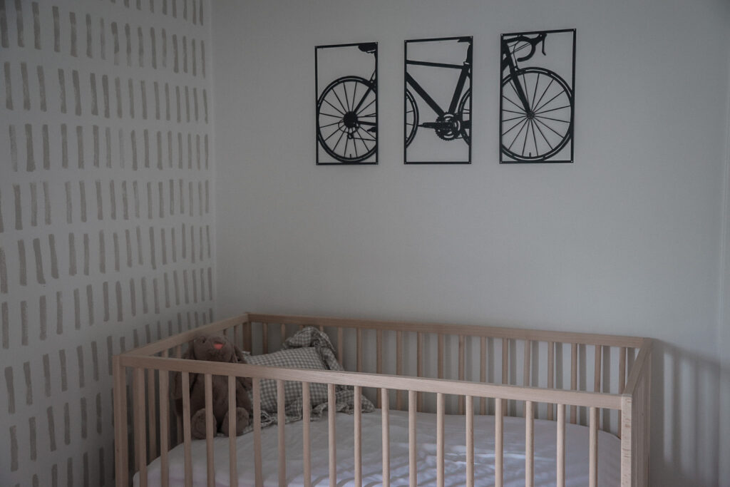 a nursery setup featuring a wooden crib with a bike picture separated into 3 frames above the bed 