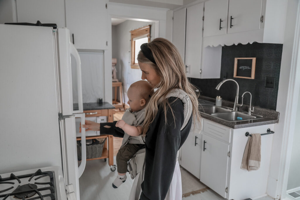 mom with baby in a front facing carrier opening the fridge