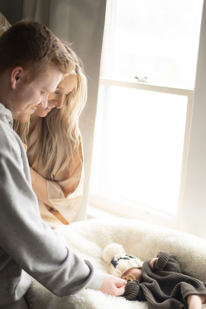 Mom and dad looking at their firstborn son lying in his bassinet by the window 