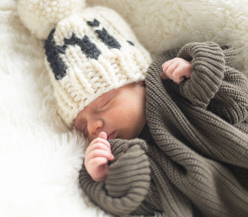 a closeup of my firstborn son sleeping in a green sweater with a cream hat on