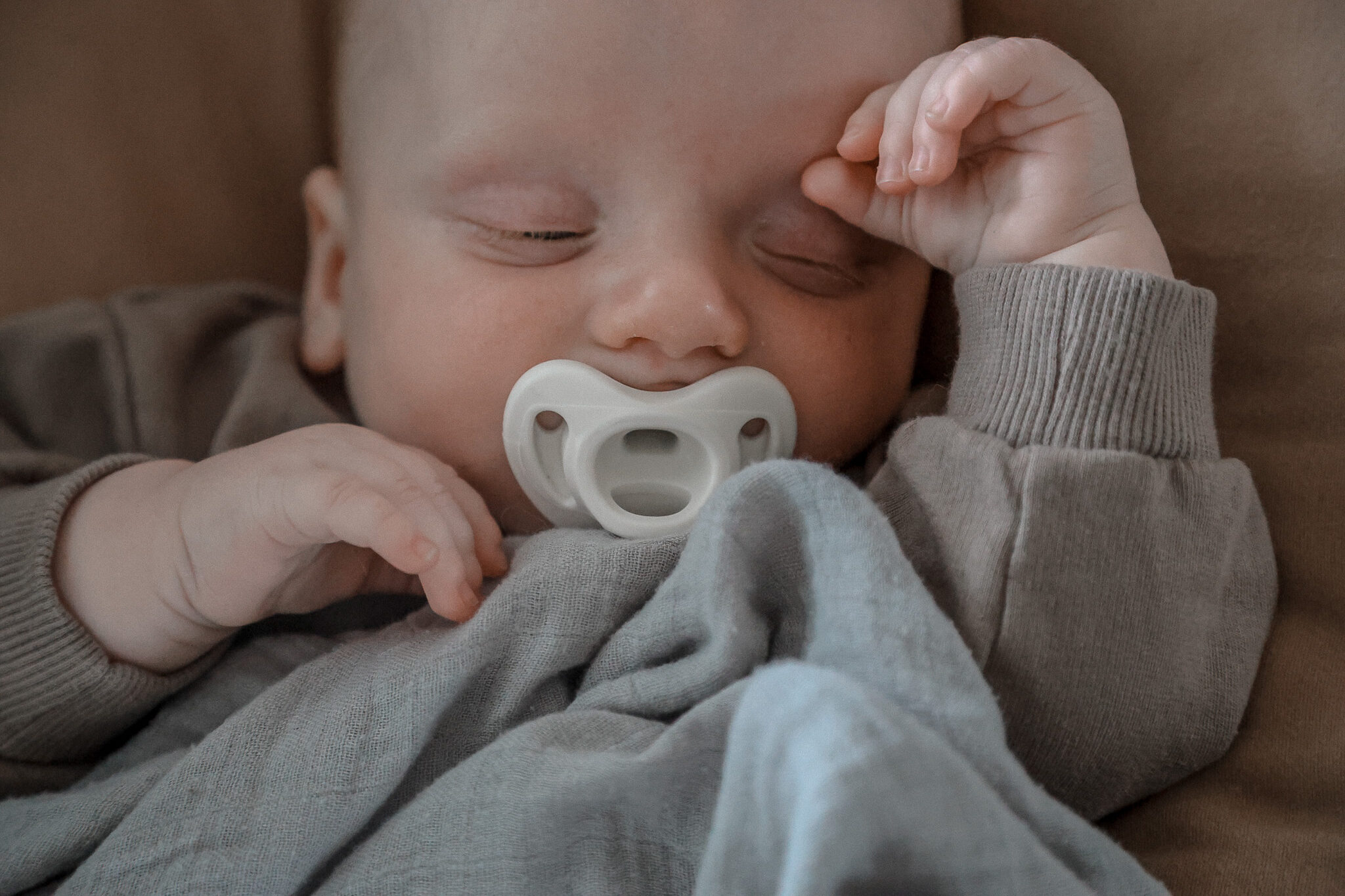 close up of a baby sleeping with his paci in his mouth and hands by his face