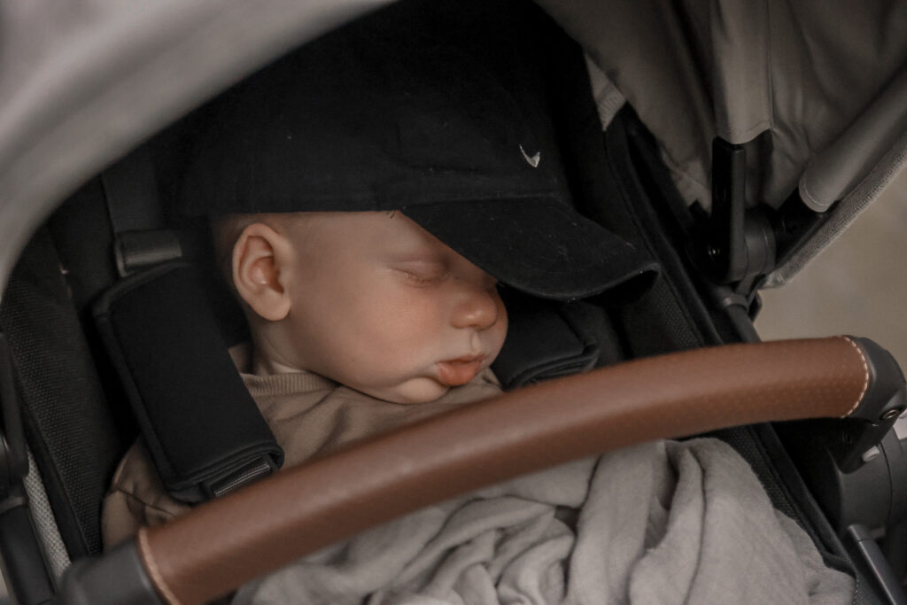 baby wearing a black Nike hat sleeping in his stroller