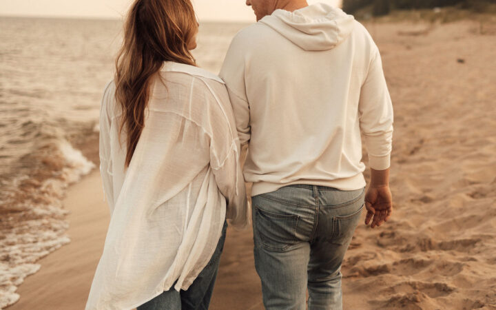 Husband and wife holding hands walking away from the camera on the beach