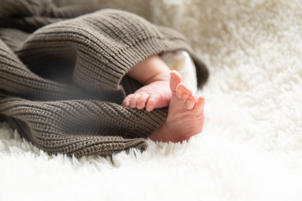 tiny new born feet sticking out of his green oversized sweater.