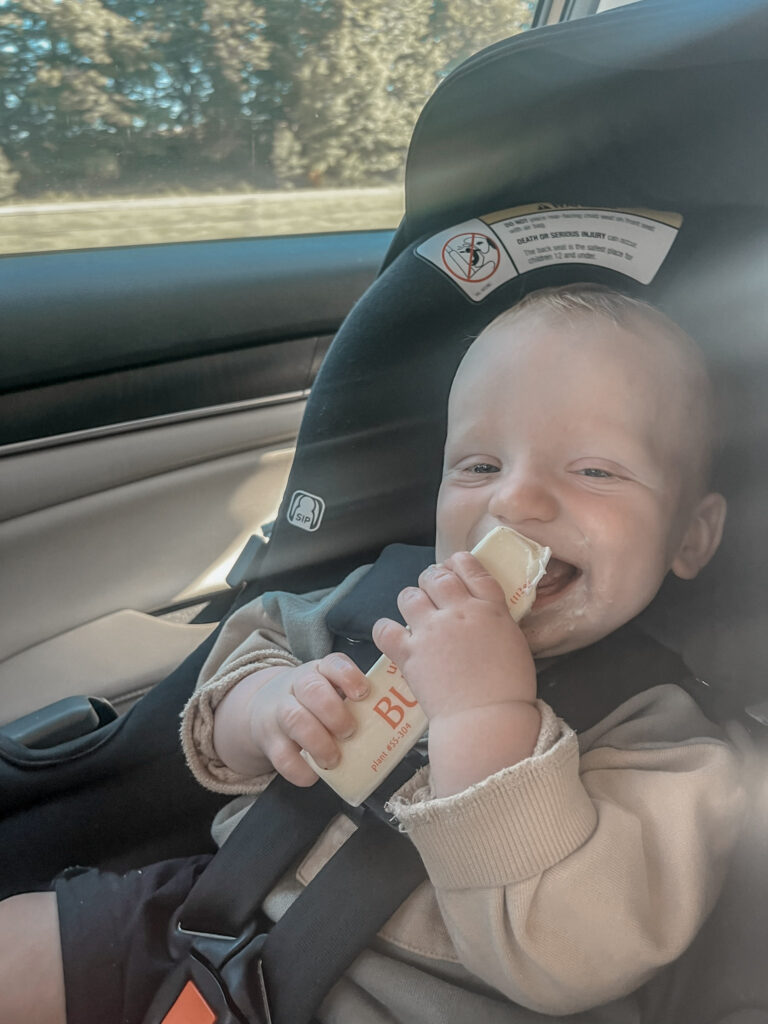 baby smiling in car seat eating a stick of butter 