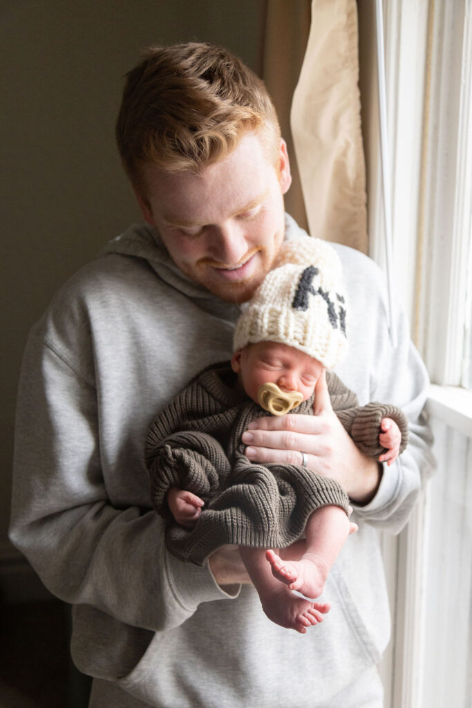 a dad holding his newborn son looking at him with a smile. 