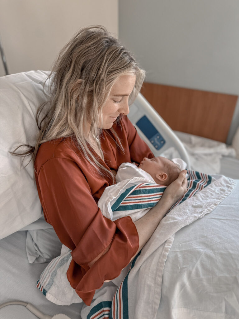 a mom sitting in her hospital bed holding her newborn baby in her arms gazing at him lovingly