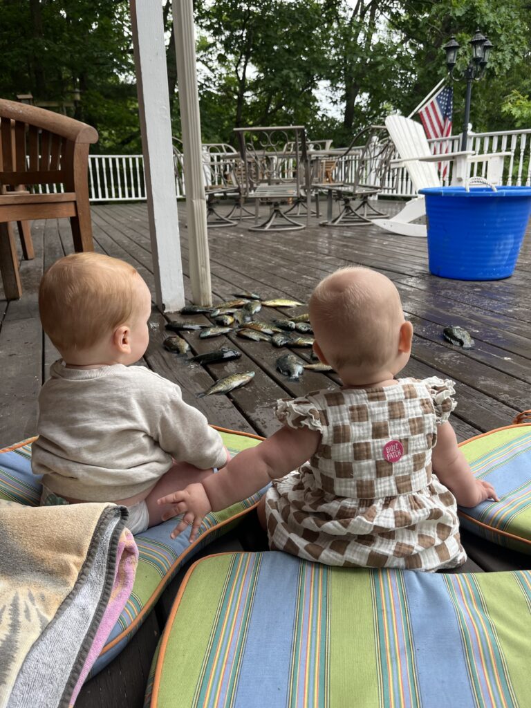 The back of 2 babies sitting up looking at a pile of fish