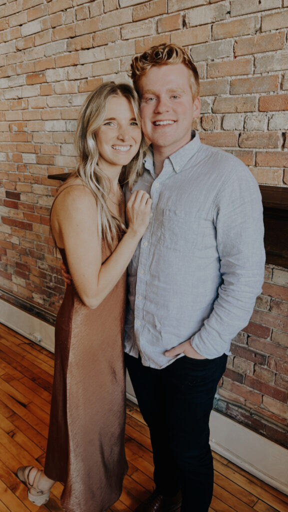 Husband and wife dressed up posing by a tan brick wall