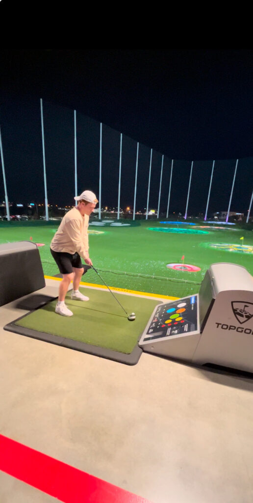 Man at top golf with backwards hat on about to hit the golf ball