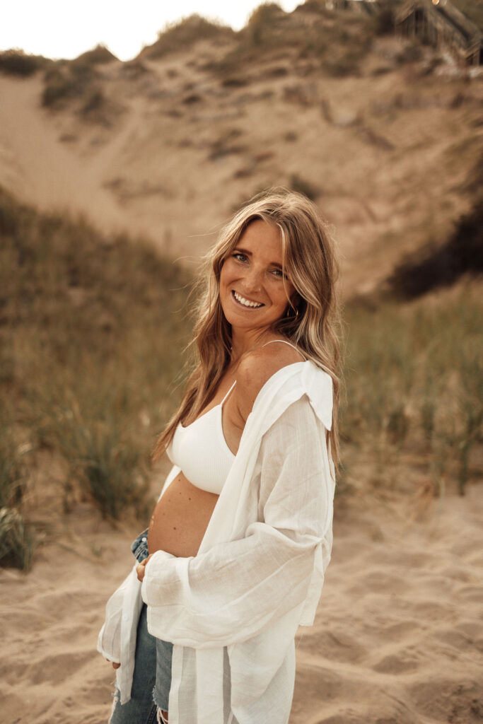Mom to be posing in sand dunes with hand on belly