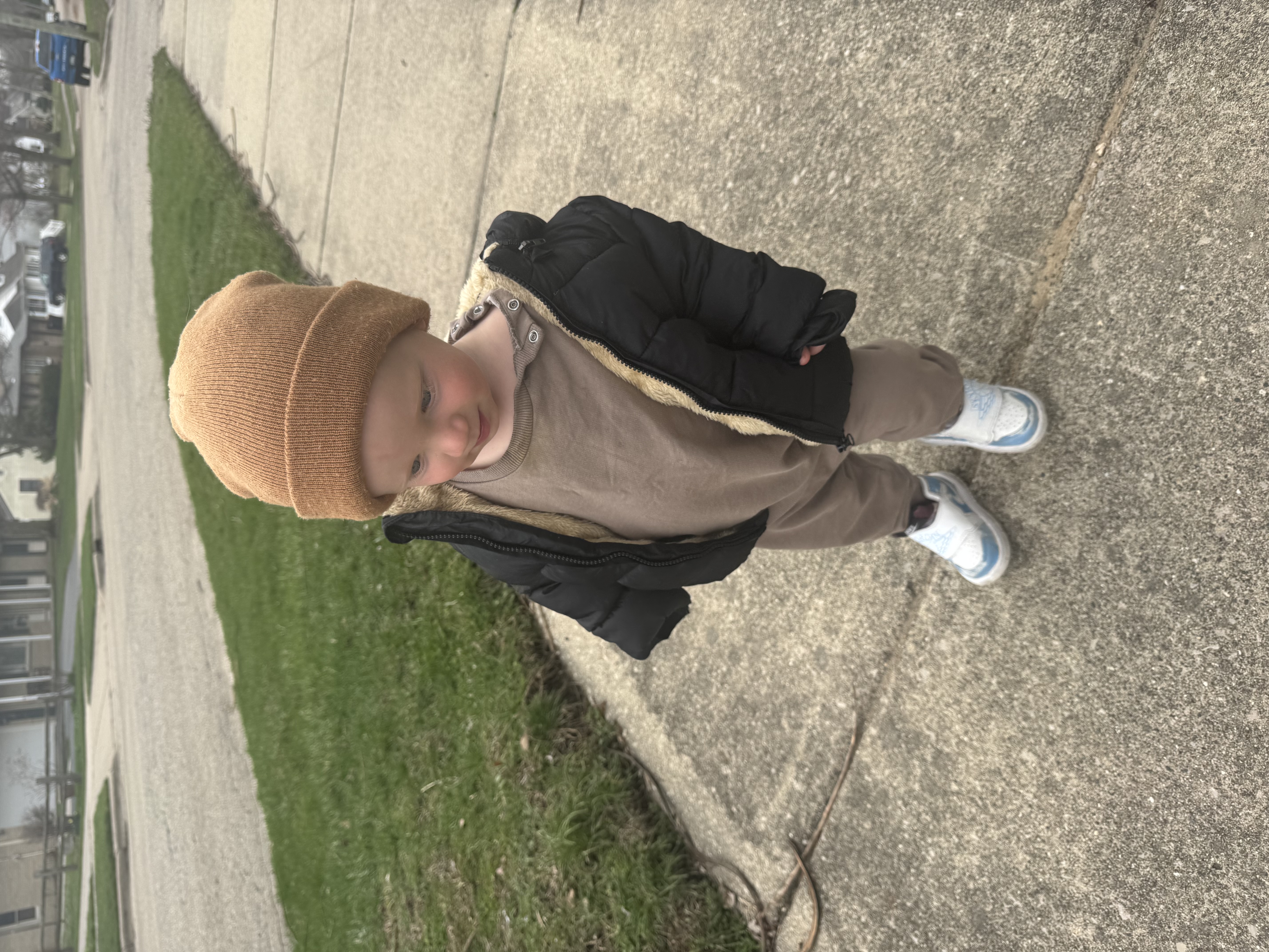 Cute baby in hat and coat walking on the sidewalk