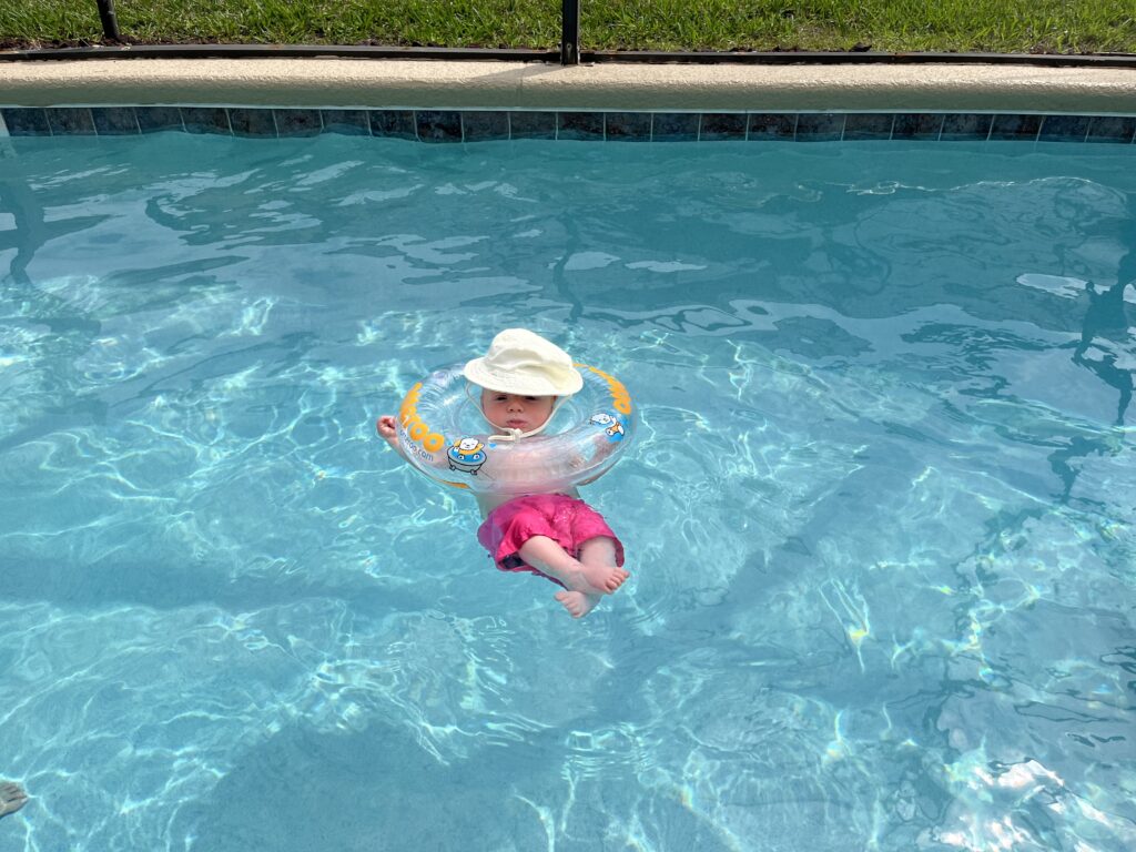 Cute baby in a pool wearing a neck floatie and a sun hat