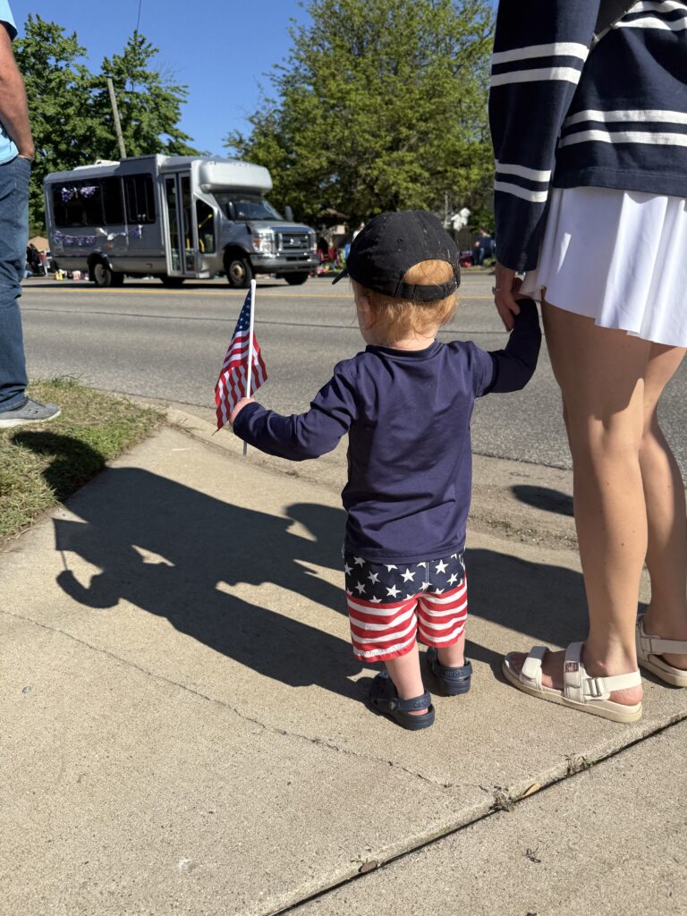 Toddler boy holding an American flag watching the 4th of July parade