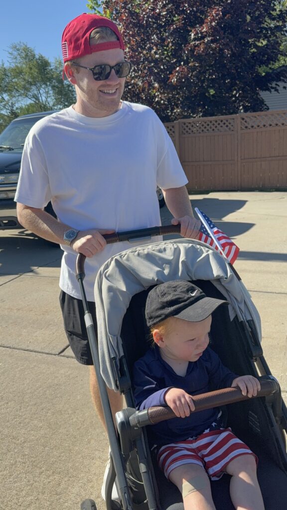 Toddler boy in his stroller watching the 4th of July parade with his dad